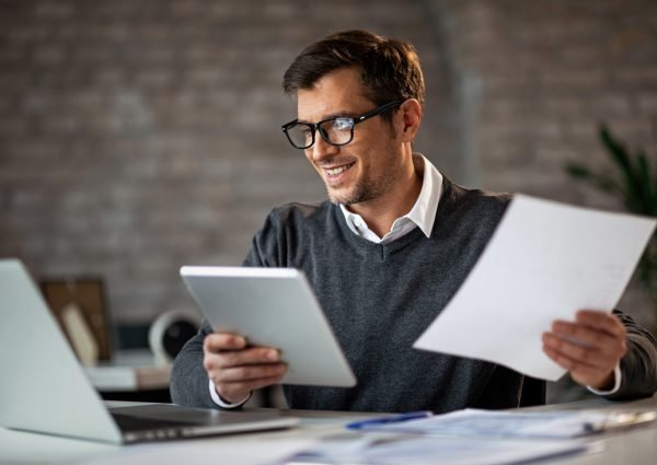 Happy businessman using touchpad and laptop while working on business reports in the office.